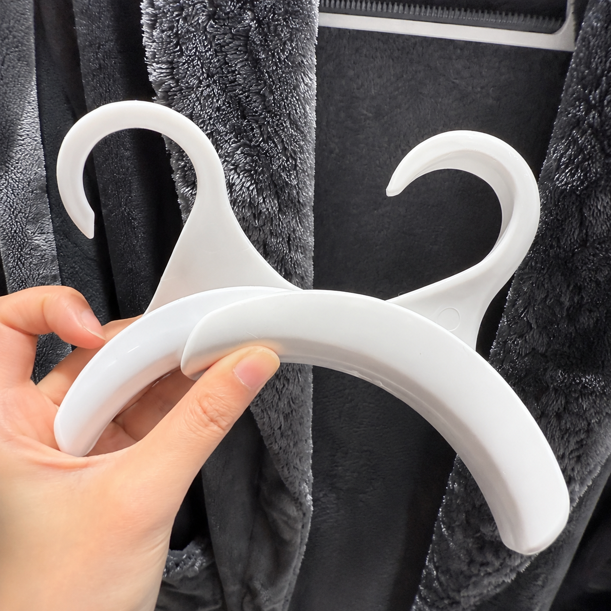 Hand holding two glossy white closet purse hooks